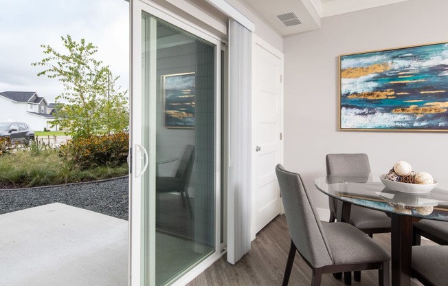 a sliding glass door opens to a patio with a dining table and chairs