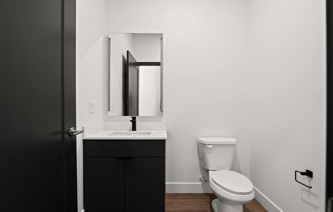 A black door is open to a white bathroom with a toilet and sink.