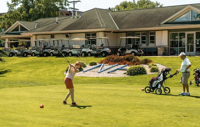 A woman is playing golf in front of a building with several golf carts.