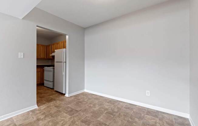 an empty living room with a refrigerator and a kitchen