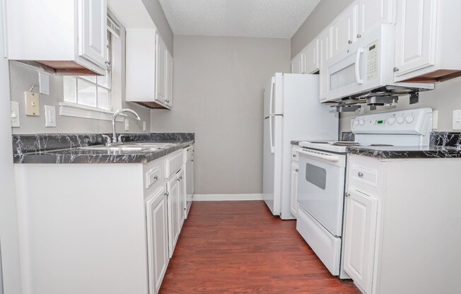 A kitchen with white cabinets, a black counter top, and wooden floors at Magnolia Apartments in Shreveport, LA