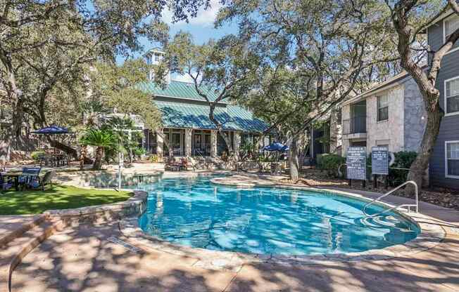 A pool surrounded by trees and a building in the background.