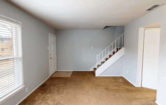 A room with a carpeted floor and a staircase.