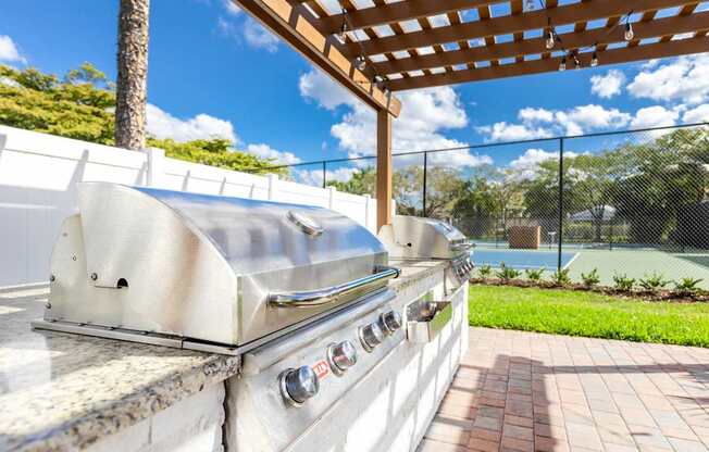 A stainless steel grill is on a patio with a wooden pergola overhead.