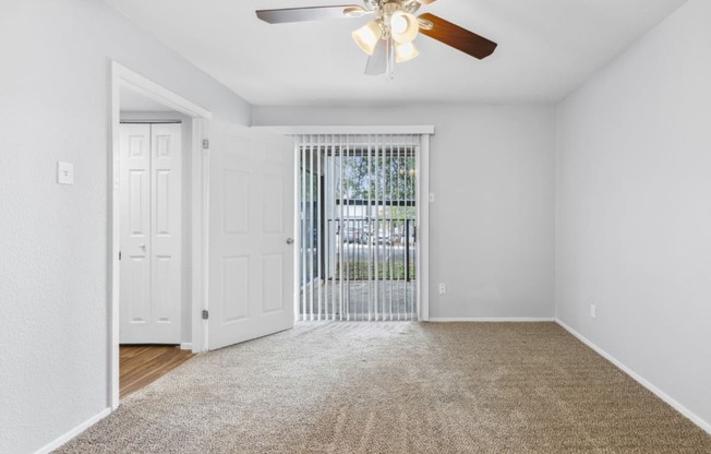 an empty living room with a ceiling fan and a door to a balcony