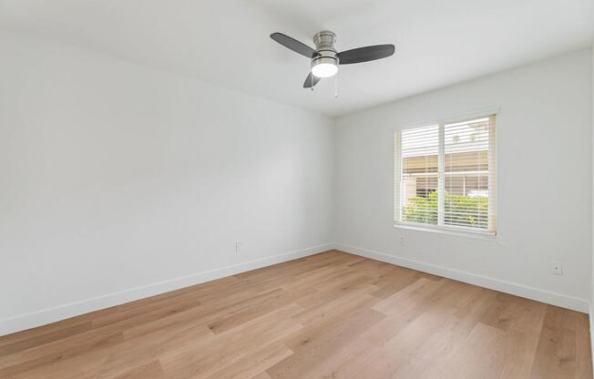 A room with a ceiling fan and a window with blinds.