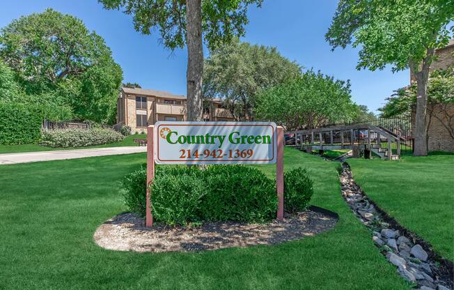 a sign over a grassy area with trees in the background