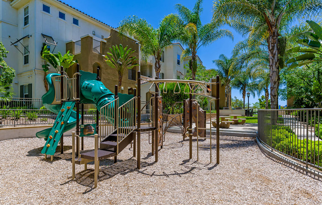 A playground with a green slide and a brown swing set.
