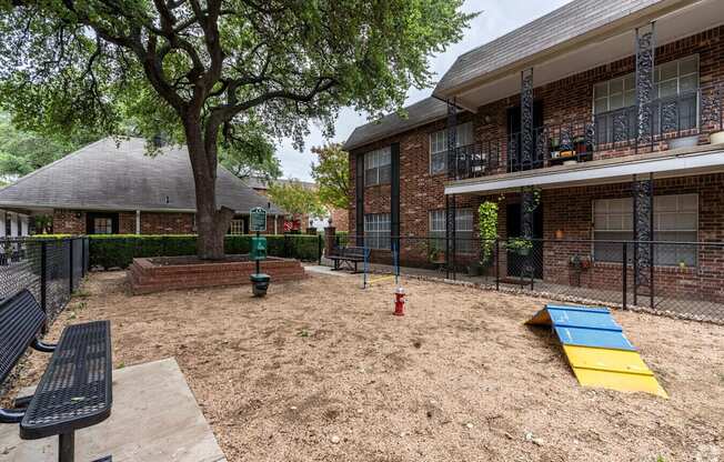 A playground area with a slide and a tree in front of a brick building.