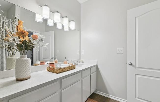 A bathroom with a vanity, a mirror, and a vase with flowers.