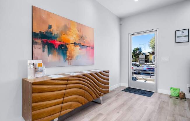 A modern waiting room with a large abstract painting on the wall and a wooden bench.
