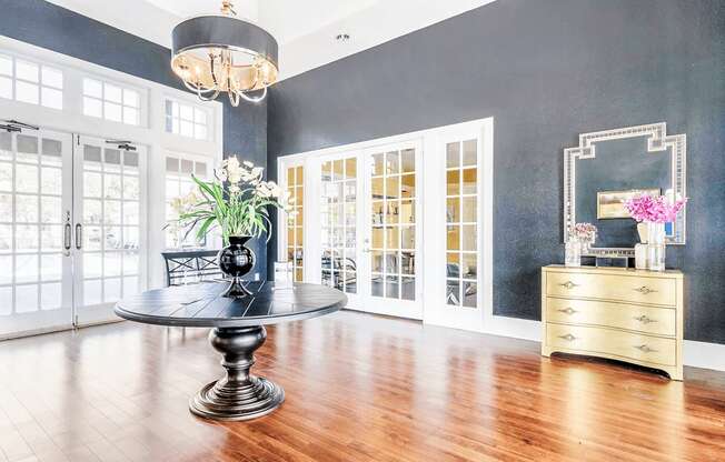 Clubhouse foyer and leasing office with a round black table, dark gray walls, wood flooring, chandelier, and large windows and doors