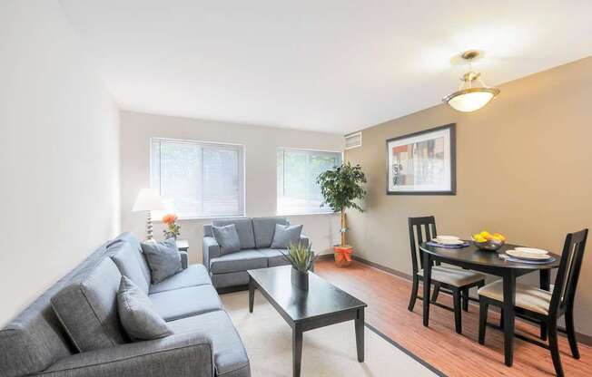 A living room with a grey couch, a black coffee table, and a dining table set for two.