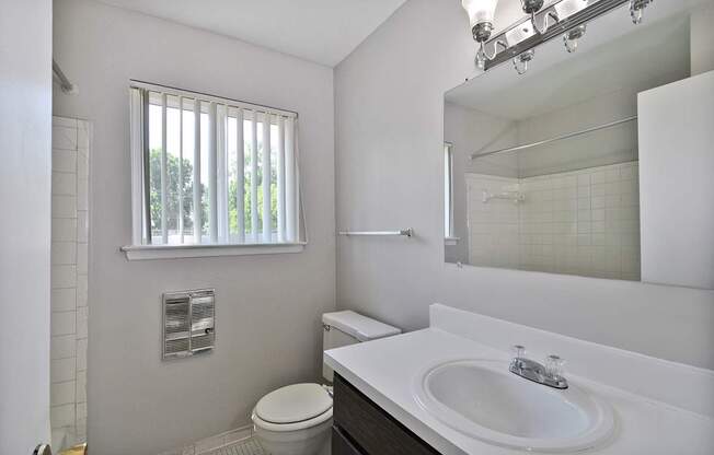 Bathroom with white vanity, framed mirror, and shower-tub combo at Warren Woods Apartments in Warren, MI.