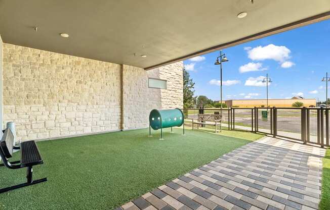 A patio area with a bench, a green trash can, and a brick wall.