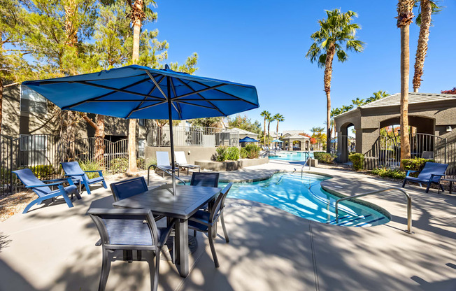 A pool area with a table and chairs and a blue umbrella.