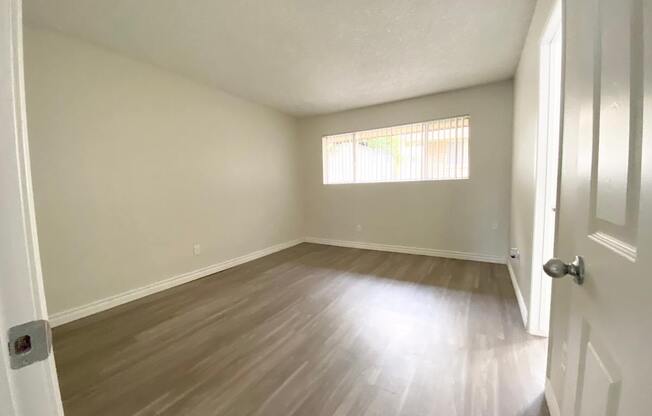 an empty living room with wood floors and a window