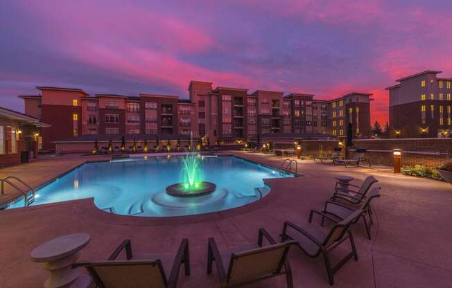 a pool with chairs and a fountain at night