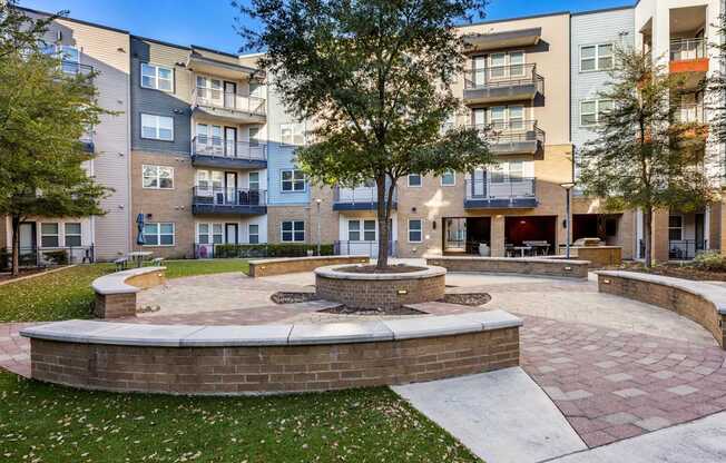A courtyard with a tree and a fire pit in front of apartment buildings.