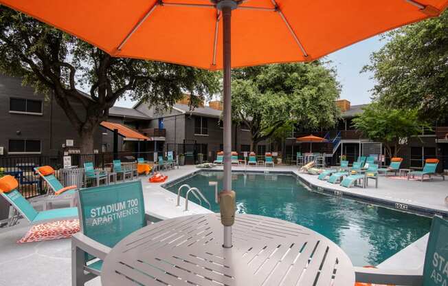 Large community pool and poolside table and chairs with orange umbrella at Stadium 700 apartments in Arlington, TX