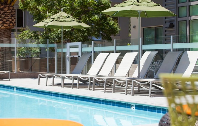 a pool with lounge chairs and umbrellas in front of a building