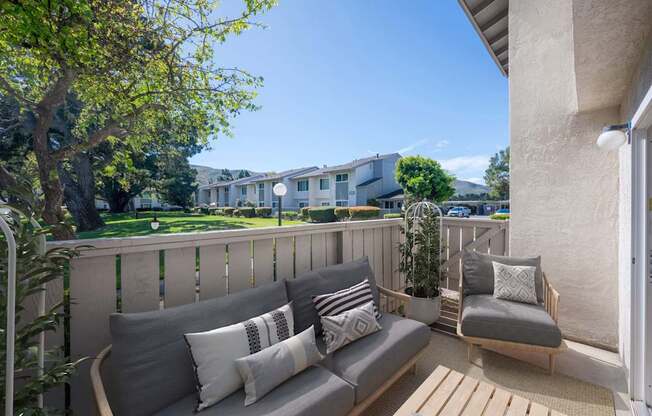 A balcony with a grey couch and pillows overlooking a building.