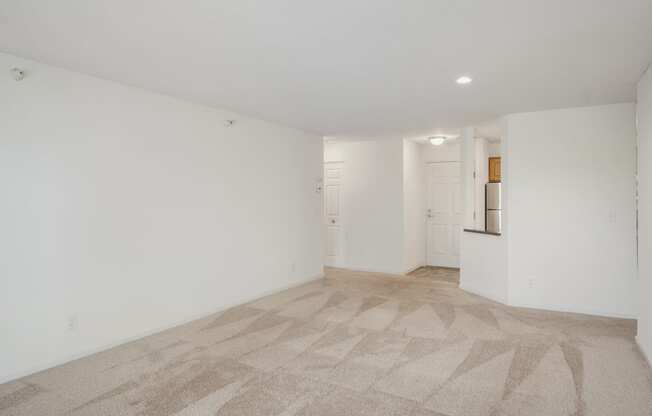 the living room and kitchen of an apartment with white walls and flooring