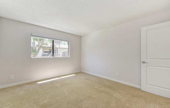 A vacant apartment bedroom with carpet and a window with blinds.