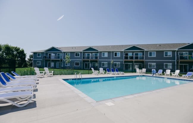 a swimming pool with chairs and a building in the background