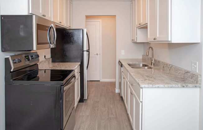 Modern kitchen with white cabinetry, stainless steel appliances, and vinyl wood style flooring throughout kitchen into the dining room.