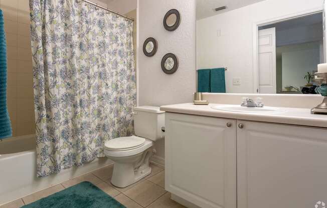 A white bathroom with a floral shower curtain and a green rug.