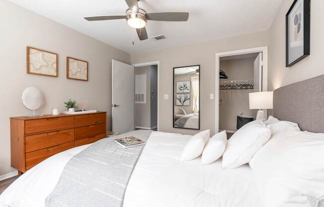A bedroom with a large bed, a ceiling fan, and a dresser.