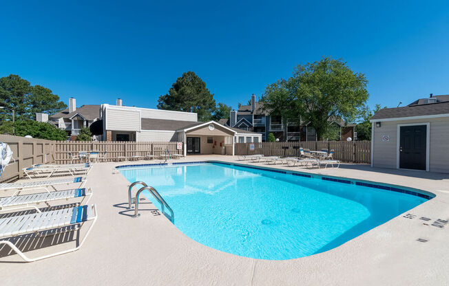 A swimming pool with sun loungers and a building in the background.
