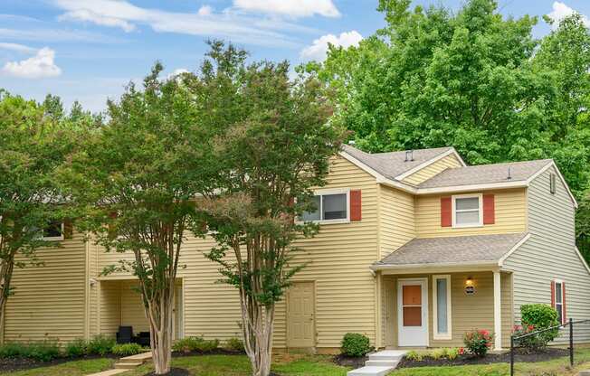 A yellow house with a red door and a small porch.