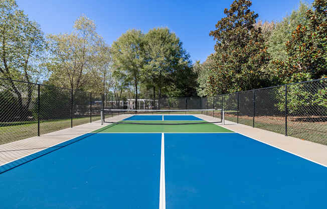 A blue tennis court surrounded by a fence and trees.