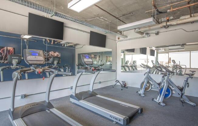 A gym with treadmills, exercise bikes, and a television.