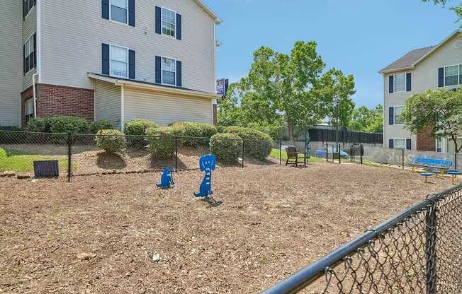 A playground with a blue slide and a fence in front of apartment buildings.