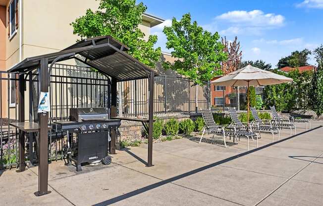 Amenity space with 4-burner gas grill under a canopy next to chaise loungers at The Residences at Toscana Park in Granger, Indiana.