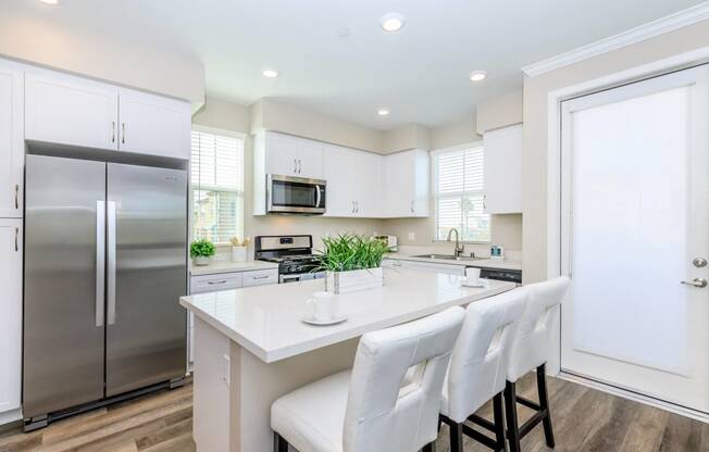 a white kitchen with stainless steel appliances and white chairs