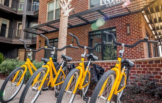 A row of yellow bicycles are parked in front of a brick building.