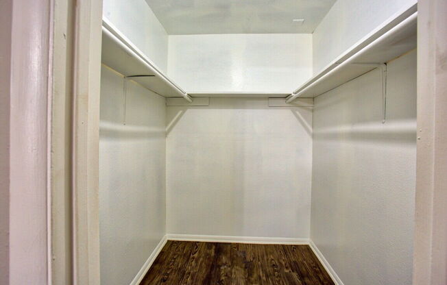 a walk in closet with white walls and a wood floor