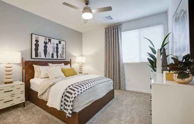 One-Bedroom Apartments in South Scottsdale, AZ - Lucent Scottsdale - Spacious Bedroom With Carpeted Flooring, Bed, Nightstands With Lamps, White Dresser, Ceiling Fan, And Window With Blinds.