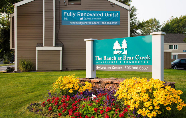A sign for The Ranch at Bear Creek Apartments & Townhomes is displayed in front of a building.
