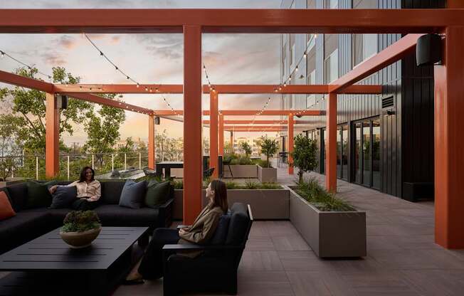Two women are sitting on a couch under a pergola.