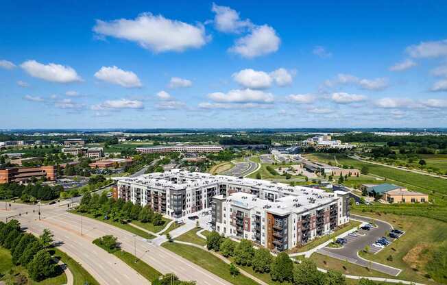 A large, modern building complex is surrounded by a green landscape and a roadway.