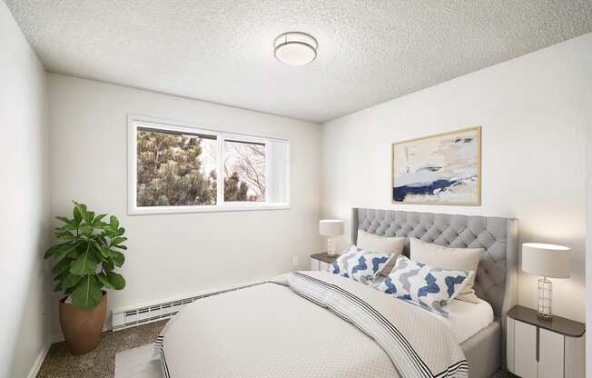 A bedroom with white walls, overhead lighting, and a window on the left wall. Staged with a bed, 2 side tables, a plant, and a rug.at Wildflower, Kennewick Washington