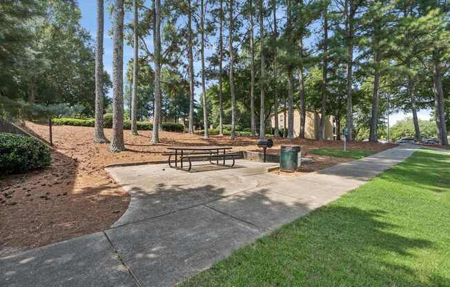 A park with a bench and a trash can.