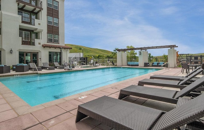 a swimming pool with chaise lounge chairs and a building in the background