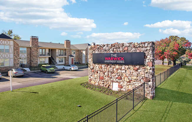 The Warwick Apartment Homes sign is made of stone and is in front of a grassy area.