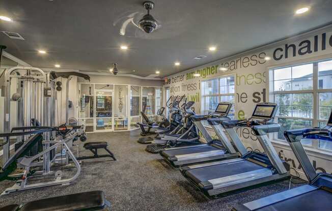 a gym with cardio machines and weights in a room with windows